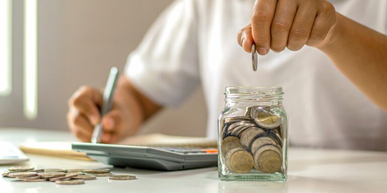 Somebody putting coins in a jar, using a calculator.
