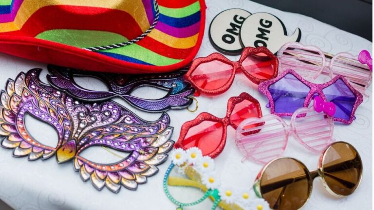Various photo booth props on a sheet, including fun sparkly star, heart and lips shaped glasses, masquerade masks, and a rainbow coloured cowboy hat.