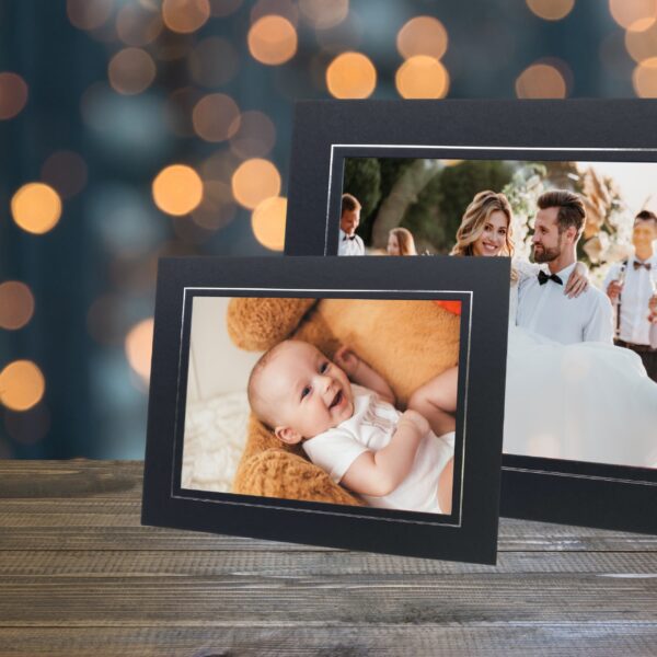Two photo mounts on a table, one with a picture of a baby laying on a giant teddy bear, and the other of a groom carrying his bride.