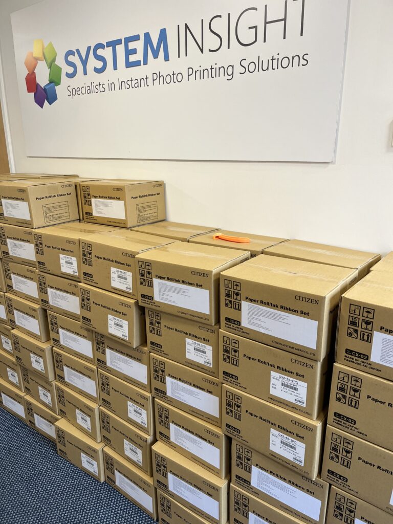 Boxes of Citizen media piled up against a wall with a System Insight logo banner.
